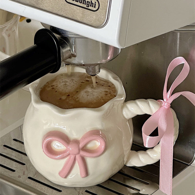 De'Longhi coffee machine pouring coffee into a white ceramic pot with a pink bow design.